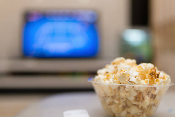 istock popcorn and remote control on sofa with a TV at background 944767178