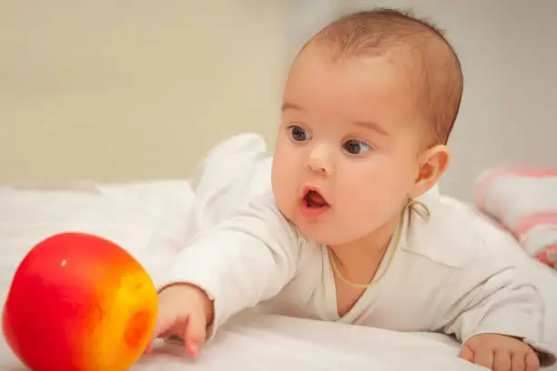 month old baby lying inbed with apple