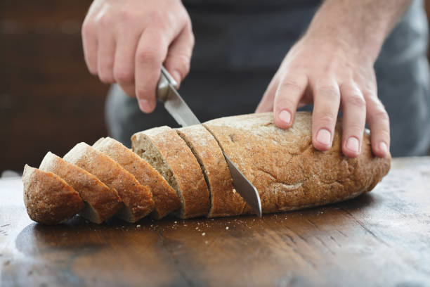 istock Close up male hands chopped fresh bread on wooden table 944774512