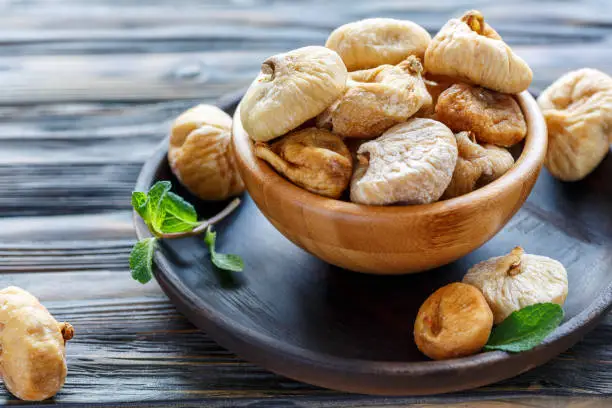 Sweet dried figs in a bowl on wooden table, selective focus.