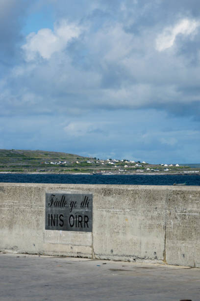Welcome to Inisheer The welcome sign on ferry dock at Caherard, Inisheer, Aran Islands, County Galway, Republic of Ireland.  Signage within the Gaeltacht (Irish speaking region) is in the Irish language.  This is a view from the dock looking west across the Inisheer coast, homes set in the burren landscape of the island. Inisheer, Aran Islands, County Galway, Republic of Ireland michael stephen wills aran stock pictures, royalty-free photos & images