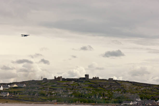 View of Inisheer from Doolin Ferry with O'Brian's Castle, airplane and bonfire. Looking southwest toward Inisheer as the Doolin Ferry approaches the dock at Caherard.  O'Brian's Castle on the hill summit.  On upper left, a small airplane taking off from the island airport.  There is smoke from a small bonfire at lower right near the ferry dock. michael stephen wills aran stock pictures, royalty-free photos & images