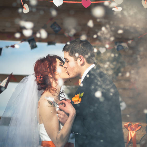 Wedding snowboarders couple just married at mountain. Husband wearng a jacket, shirt, butterfly, trousers. Bride dressed in white dress. Wedding ceremony at alps mountains at winter with snowboards