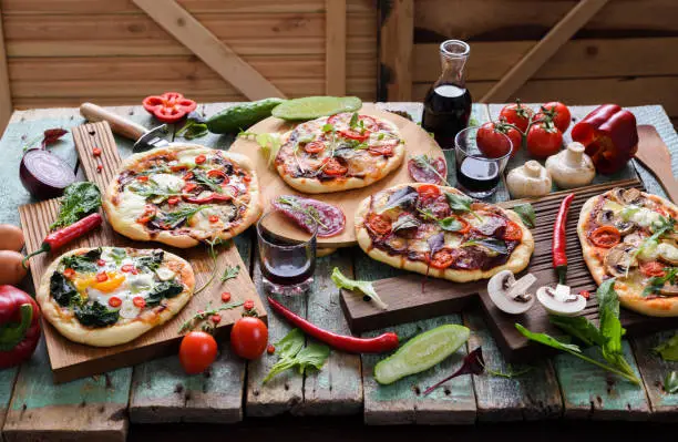 Pizza and wine party. Pizzas and raw vegetables in abundance on oak chopping boards over shabby blue wooden background horizontal