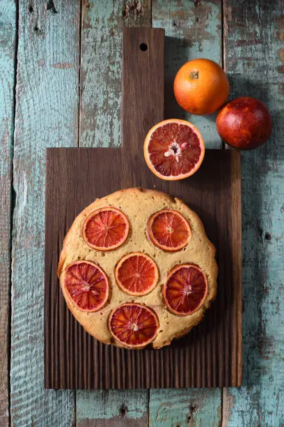 Dark oak board with round homemade fruit cake and blood oranges on shabby blue background top view