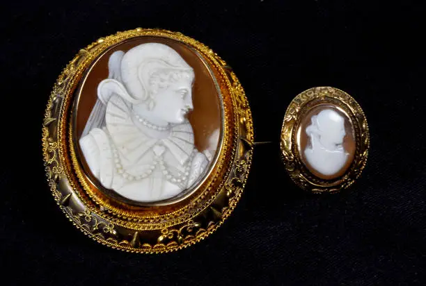 Brown and Gold Antique Cameo Brooch with white carved face with a matching ring on a black background