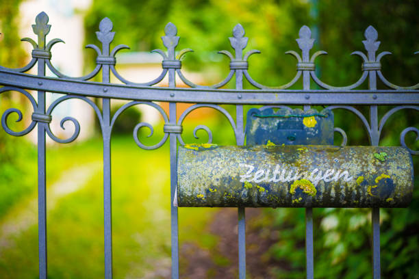 Mailbox for newspapers, iron gate and house out of focus
