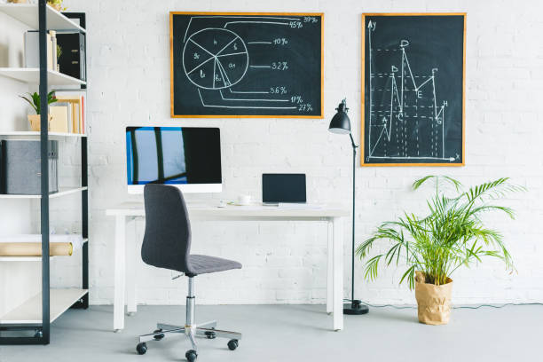 istock Computers on table in light office with business charts on walls 944840754