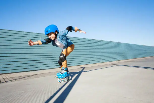 Side view portrait of preteen boy, roller skater in helmet and protective gear, skating fast at outdoor rollerdrom