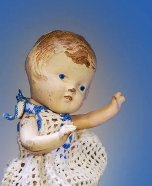 Antique cracked and worn baby doll in blue and white crochet dress against blue background
