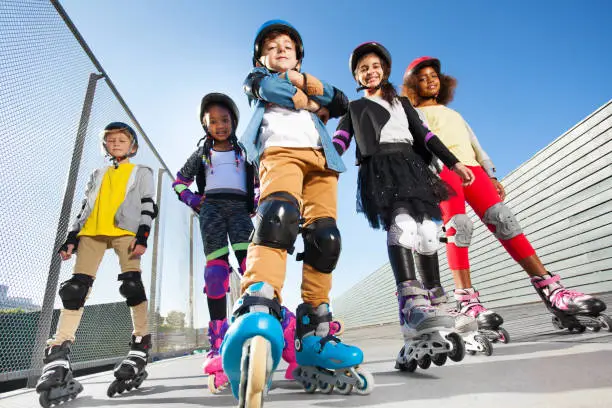 Bottom view portrait of happy boy in rollerblades and protective gear standing with friends outdoors at stadium