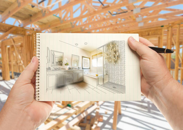 istock Hands Holding Pen and Pad of Paper with Bathroom Design Inside House Construction Framing. 944867932