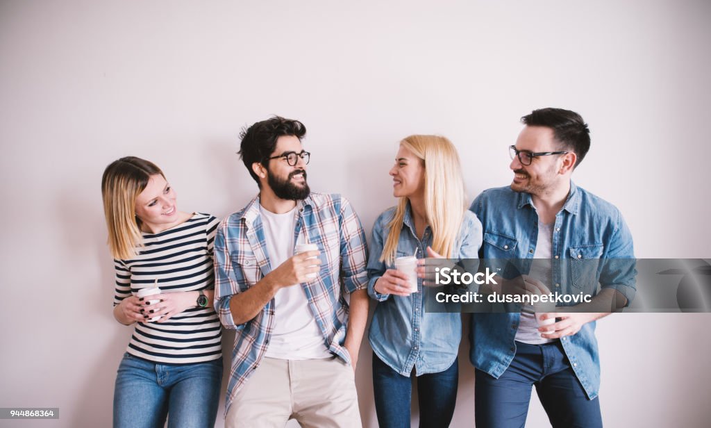 Grupo de elegante feliz jovens encostado na parede e falar enquanto café bebidas no copo de papel. - Foto de stock de Amizade royalty-free