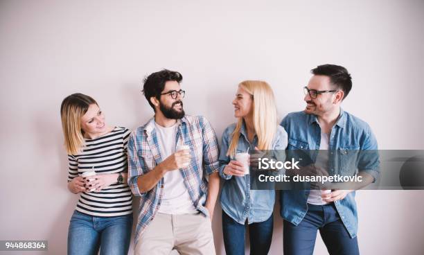 Foto de Grupo De Elegante Feliz Jovens Encostado Na Parede E Falar Enquanto Café Bebidas No Copo De Papel e mais fotos de stock de Amizade