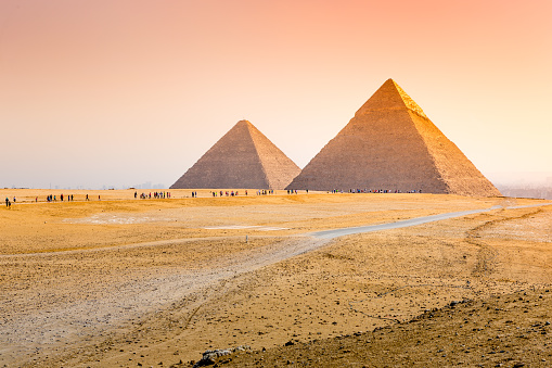 Beautiful young woman having a video call in front of the Pyramids of Giza (Egyptian pyramids) in Cairo, Egypt.