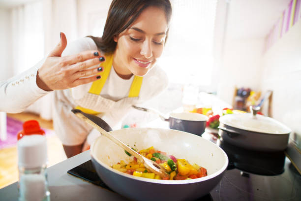 young charming pretty woman is smiling while smelling the aroma of her fresh healthy breakfast being cooked. - food prepared potato vegetable healthy eating imagens e fotografias de stock