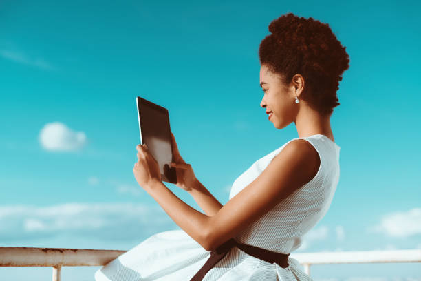 istock Black cheerful girl with digital tablet and sky behind 944875534