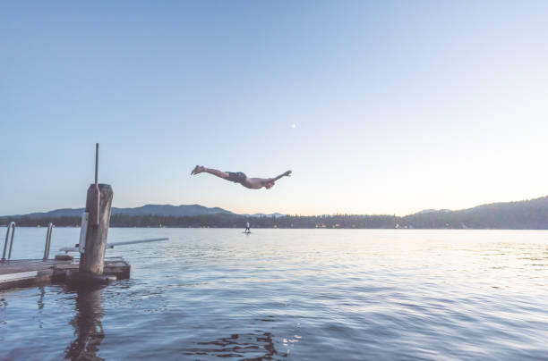 istock Young man dives into a lake off pier at dusk 944882668