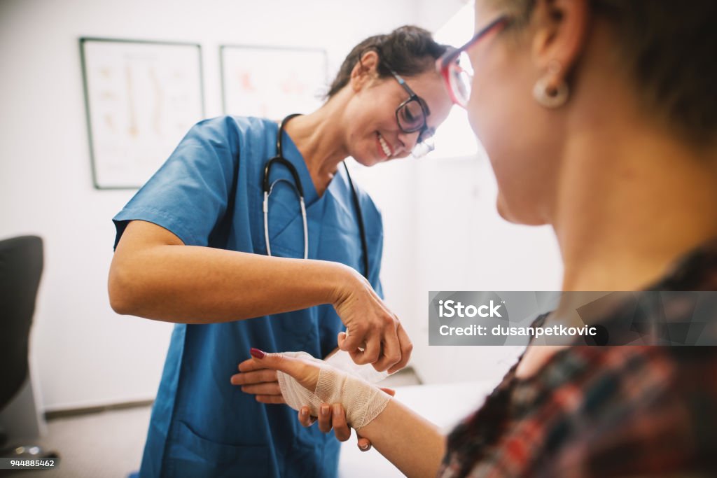Infermiera professionista in ospedale che fascia la mano con una benda medica per una paziente donna. - Foto stock royalty-free di Infermiere