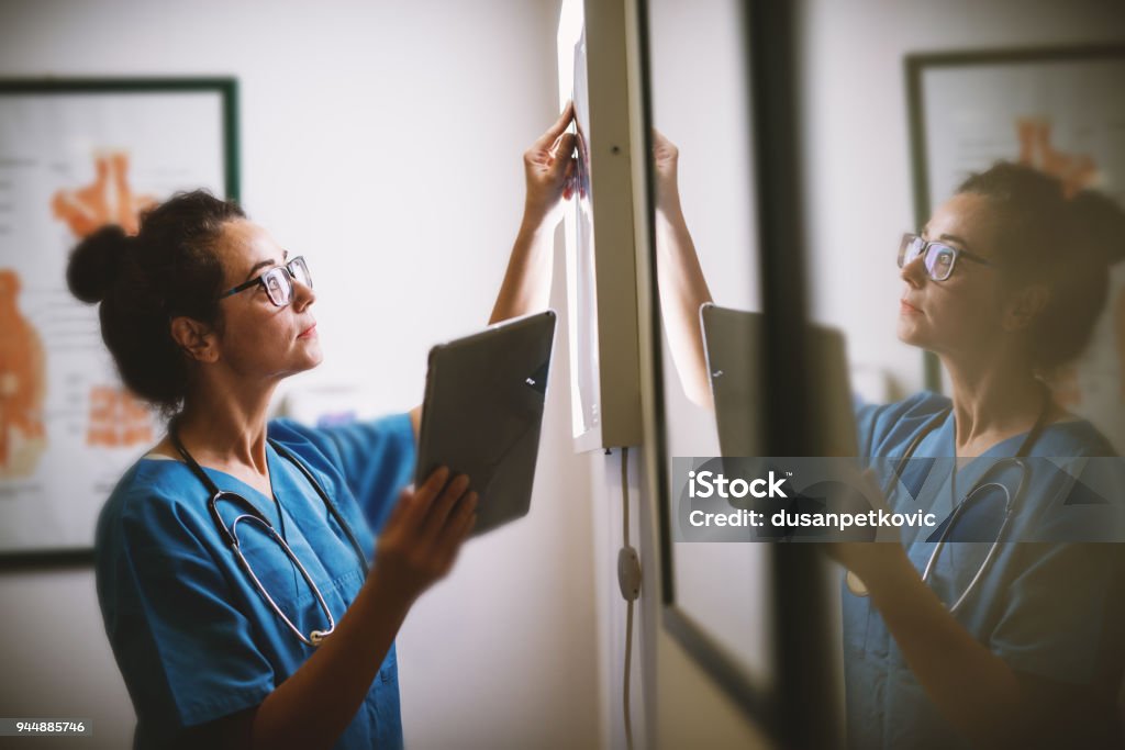 Vue latérale du sourire milieu ans infirmière contrôle aux rayons x dans un docto - Photo de Suivi des malades libre de droits