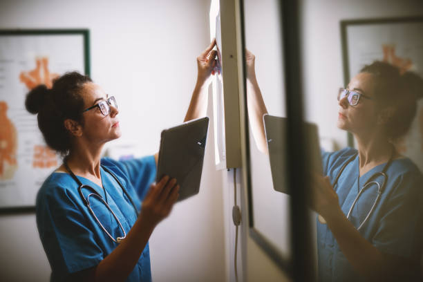 Side view of smiling middle aged nurse checking X-ray in a docto Side view of smiling middle aged nurse checking X-ray in a doctors office. x ray equipment stock pictures, royalty-free photos & images