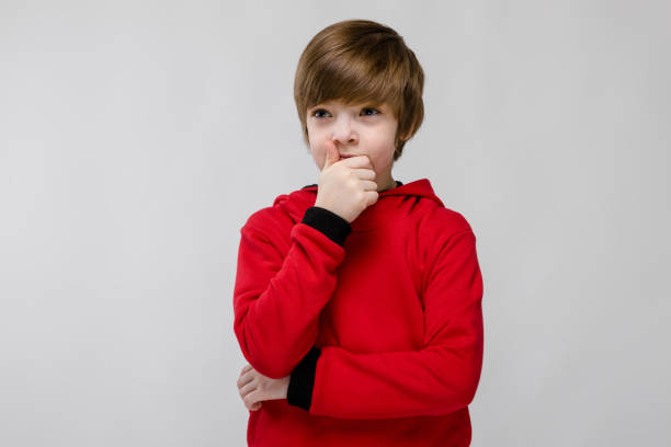 istock Cute confident caucasian little boy in red sweater thinking on grey background 944887184