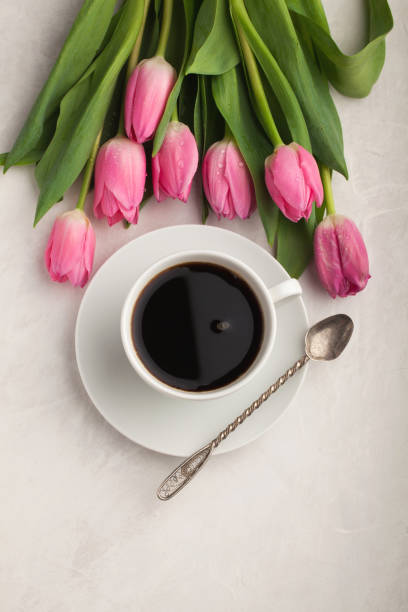 istock Black coffee in white Cup with pink tulips on light stone background. Top view with copy space 944889486