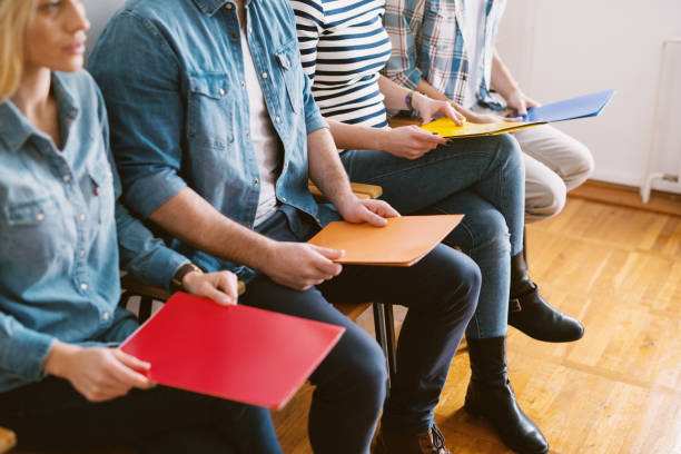 cerrar vista de jóvenes entrevista personas sentadas en sillas con carpetas antes de la tarea en la sala de espera. - unemployment fotografías e imágenes de stock