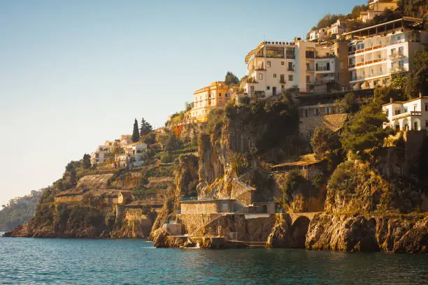 White Italian villas perched above the sea in warm sunset light