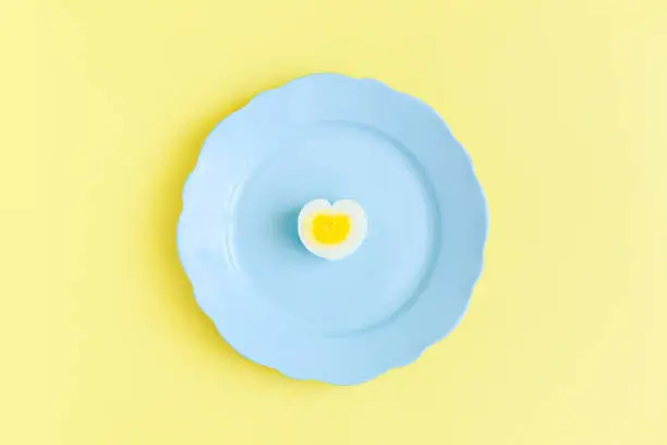 Half a boiled egg, in the shape of a heart on a blue plate on a yellow background, the concept loves Easter