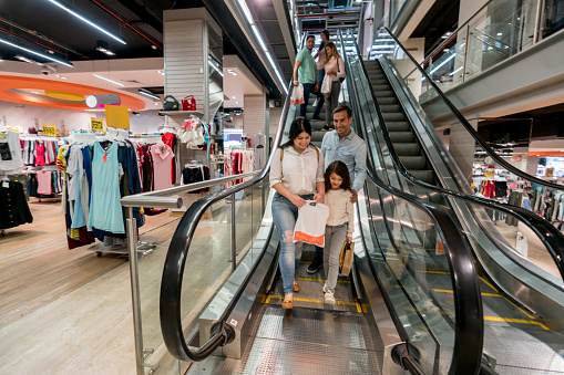 Happy shopping family going down on the escalators at a department store and smiling - lifestyle concepts