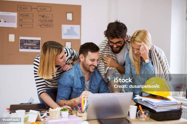 Equipo De Negocio Feliz Hermosa Joven Mirando Portátil Mientras Ríe Y Lluvia De Ideas Sus Ideas Foto de stock y más banco de imágenes de Inmobiliaria