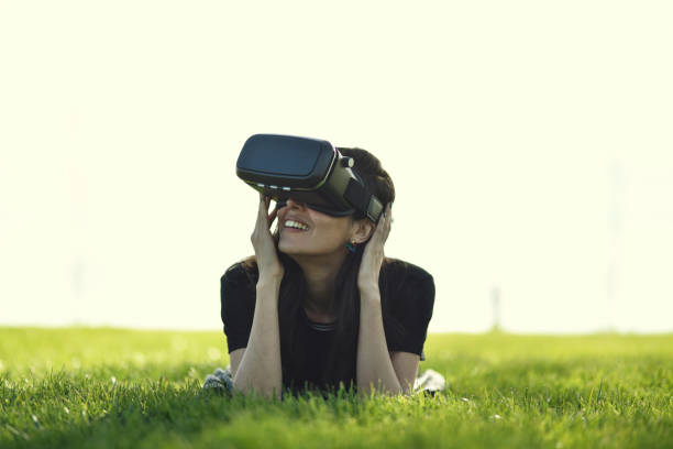 istock Young woman lying down on the grass, watching around via VR 944900504
