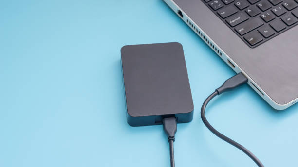 istock Black external hard disk connecting to a laptop on a blue background. 944911422