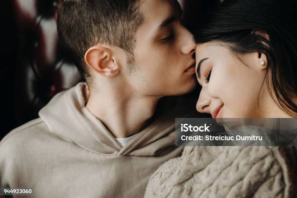 Close Up Portrait Of A Lovely Young Couple Sitting On A Leather Chair While Boy Is Kissing His Girlfriend On Forehead Stock Photo - Download Image Now