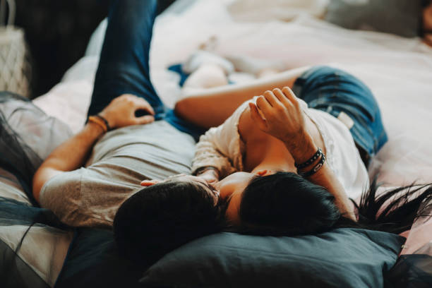 atrakcyjna romantyczna para leżąca na łóżku, przytulanie i całowanie w przytulnym pokoju. - sheet human hand bed women zdjęcia i obrazy z banku zdjęć