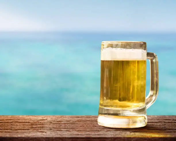 Glass of Beer on Wooden Table in front of the Sea, Blurred Blue Ocean and Sky as background