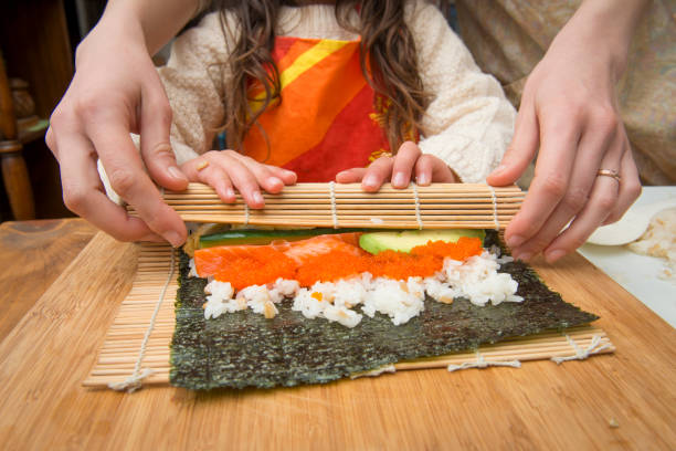istock Mother and daughter making rolled sushi 944945418