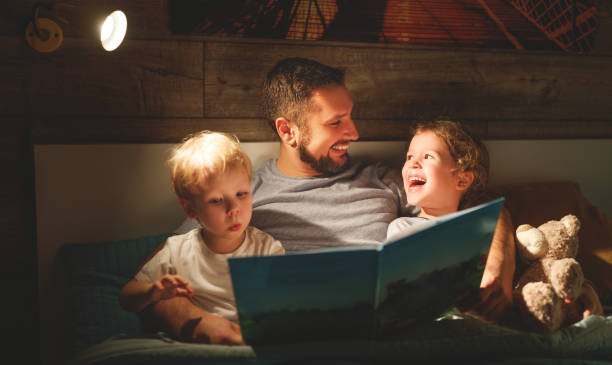 abend-familie lesen. vater liest kindern. buchen sie, bevor sie zu bett gehen - schlafenszeit stock-fotos und bilder