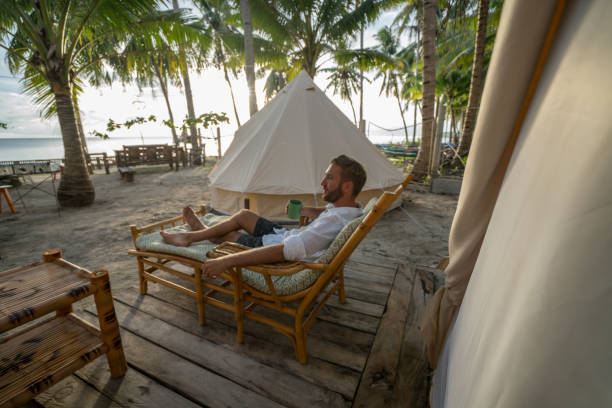 Man relaxing in glamping site in tropical Island Young man lying on sofa in front of luxury tent in clamping campsite under the coconut palm trees in the Islands of the Philippines tropical climate people relaxation vacations concept. siquijor island stock pictures, royalty-free photos & images
