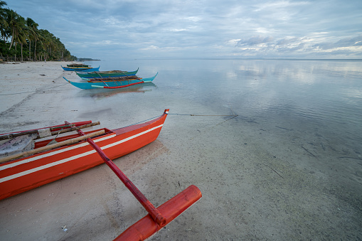 Fishing boat on beach at sunset, Philippines \nBeautiful light na sunbeam over the boat, wooden traditional Filipino boat. Travel destinations and tropical climate concept.