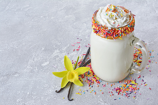 Crazy vanilla milk shake with whipped cream and colored sprinkles in glass jar on gray concrete background