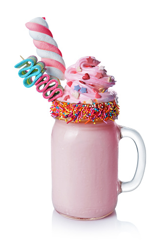 Crazy milk shake with pink whipped cream, marshmallow and colored candy in glass jar isolated on white background