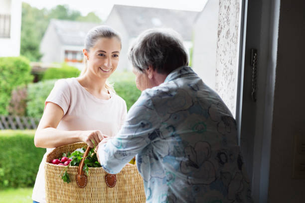 young caregiver delivers groceries to senior woman stock photo