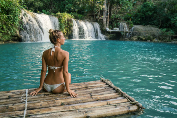 istock Young woman on bamboo raft at tropical waterfall enjoying life 944965968
