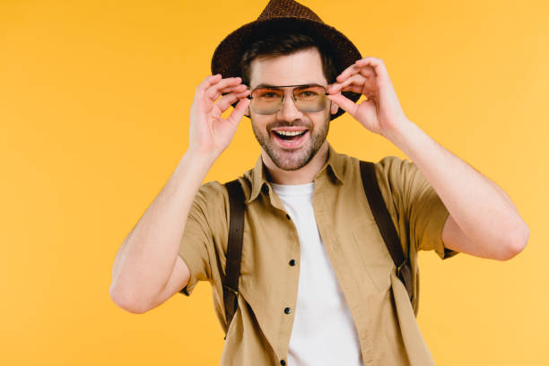 istock handsome young man in hat and sunglasses smiling at camera isolated on yellow 944969582
