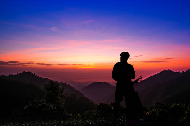 Silhouette of a young man with a bicycle at sunset sky with dramatic clouds on background