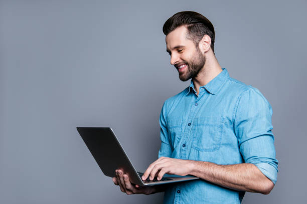 istock Smiling cheerful young man  holding laptop and typing 944976506