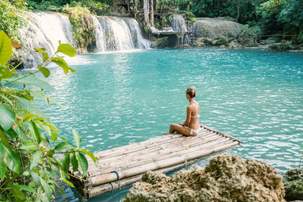 Girl contemplating beautiful waterfall in the Philippines from bamboo raft Young woman contemplating a beautiful waterfall on Siquijor Island in the Philippines. People travel nature loving concept. One person only enjoying outdoors and tranquillity in a peaceful environment, solo traveler concept siquijor stock pictures, royalty-free photos & images