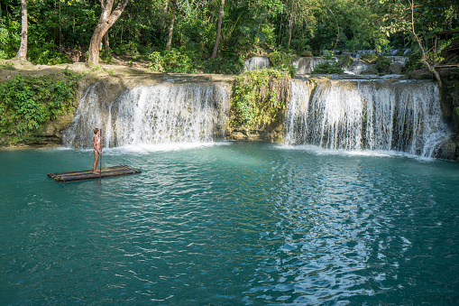Young woman bamboo rafting on a beautiful waterfall on Siquijor Island in the Philippines. People travel nature outdoor activities concept. One person only enjoying outdoors and tranquillity in a peaceful environment, solo traveler concept